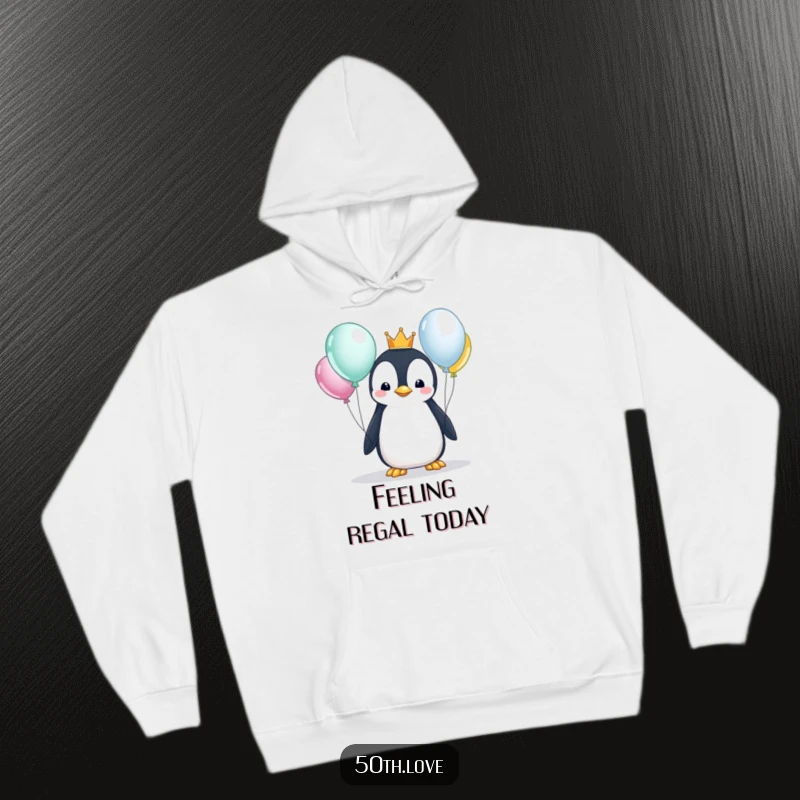 Funny penguin wearing a crown and looking at balloons, featured on a cozy hoodie, perfect for a majestic and humorous birthday celebration.