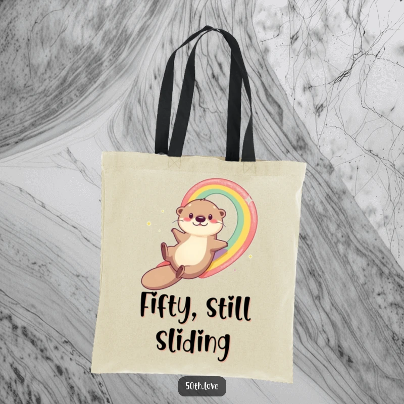 Funny otter mid-slide down a rainbow leading to number 50, on a tote bag, symbolizing a fun and adventurous 50th birthday journey.